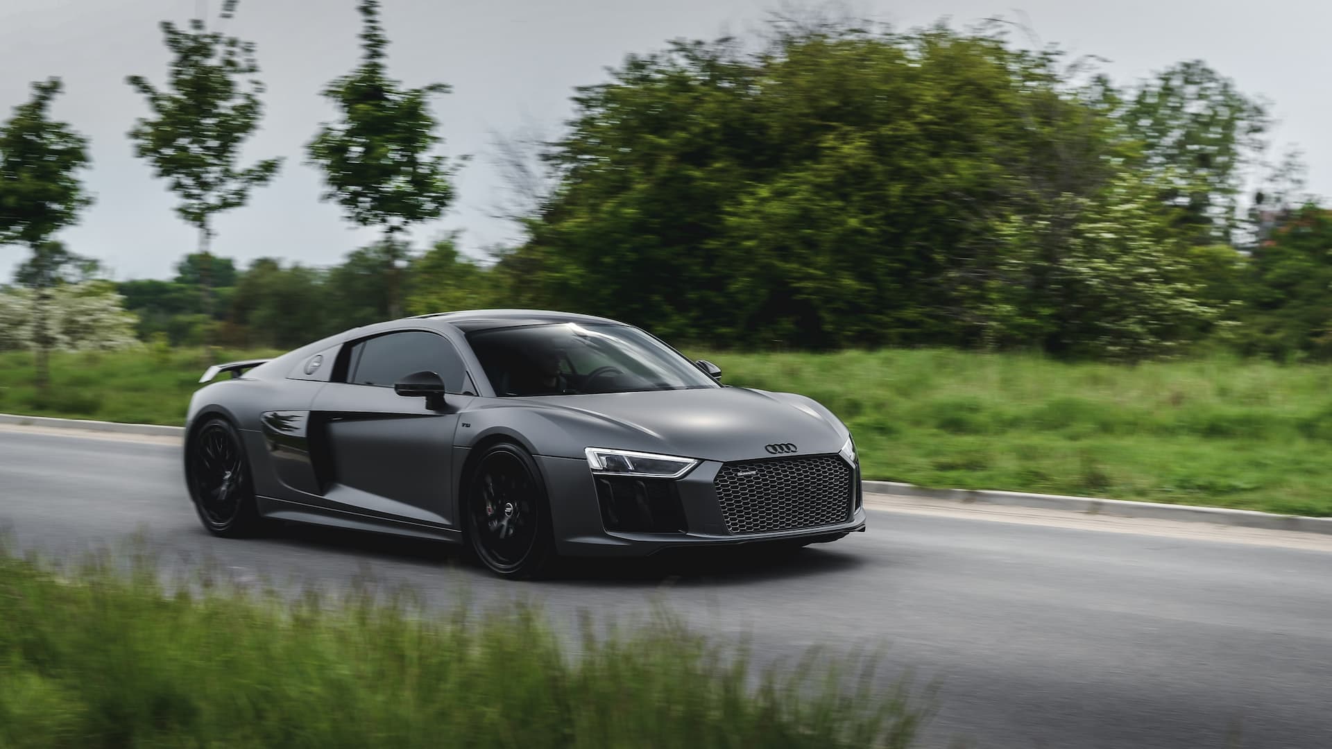 A matt Grey Audi R8 with tinted windows driving on a country road
